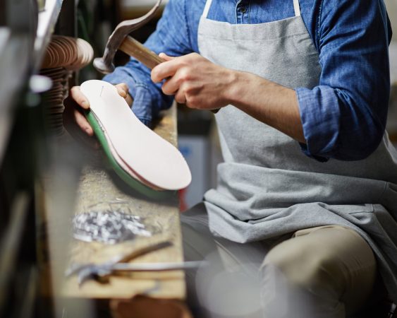 Young footwear repairman doing his work in his own workshop